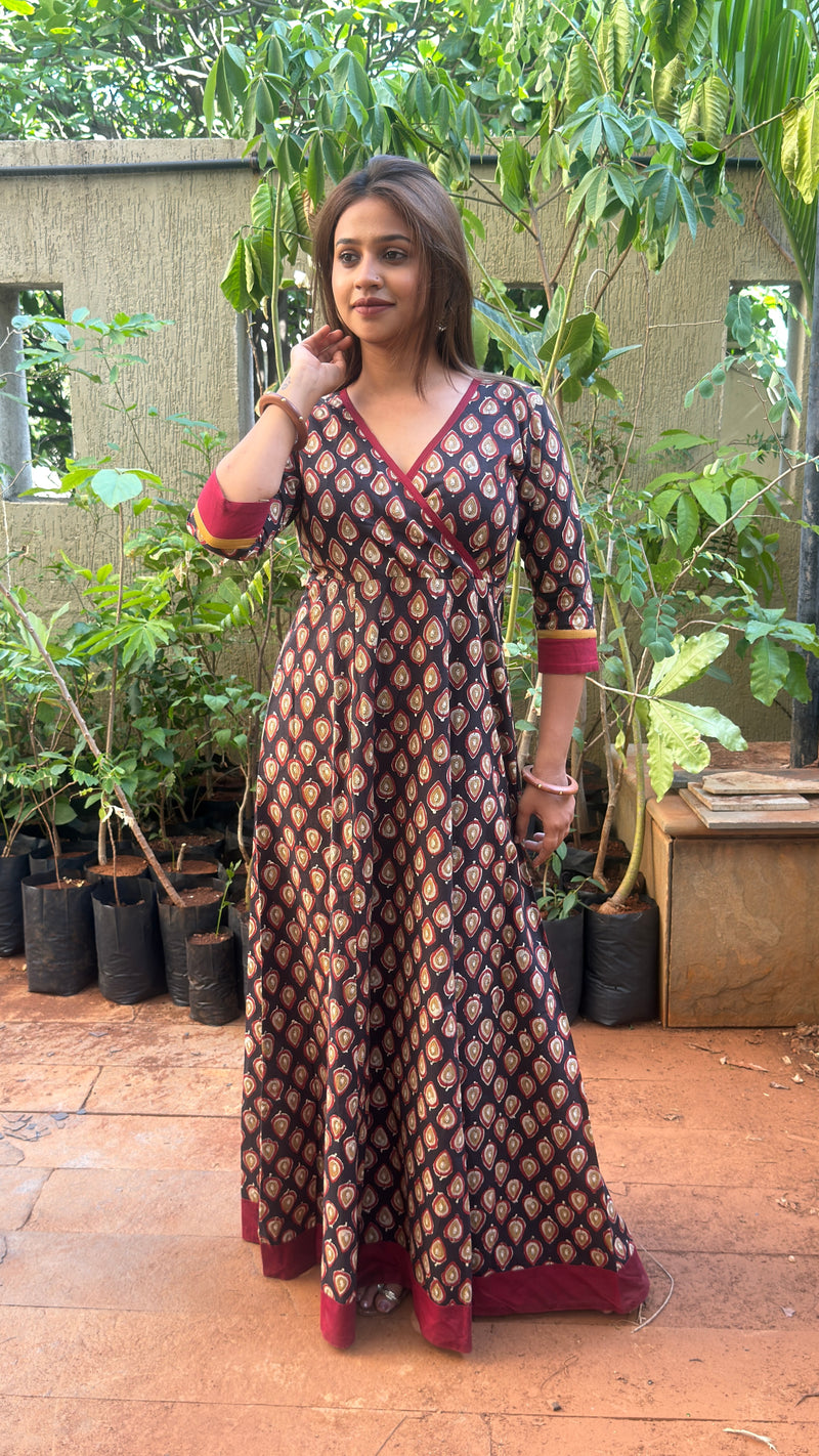 Lower body view showing the red hem border and full length of the black cotton long dress standing on stone pavement.