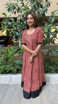 Model in red handloom cotton long dress with small white floral buti print and a black contrast hem panel, in garden setting