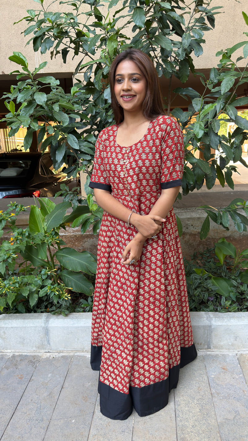 Model in red handloom cotton long dress with small white floral buti print and a black contrast hem panel, in garden setting