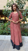Model in red Ninara long dress with black hem walking through garden path