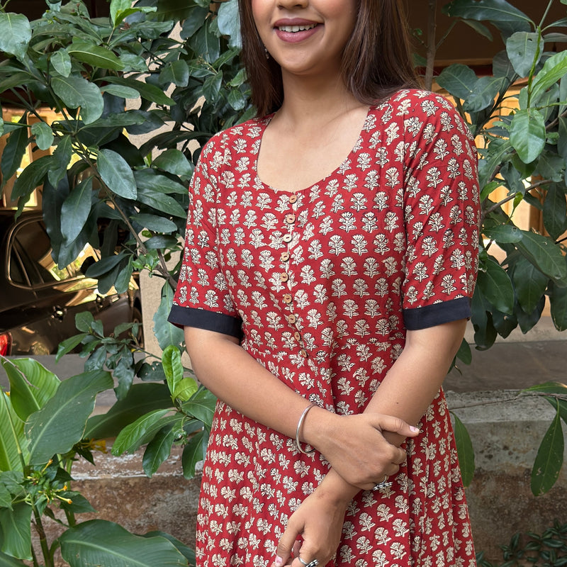 Full height portrait of the woman posing in the red cotton long dress with the black hem.