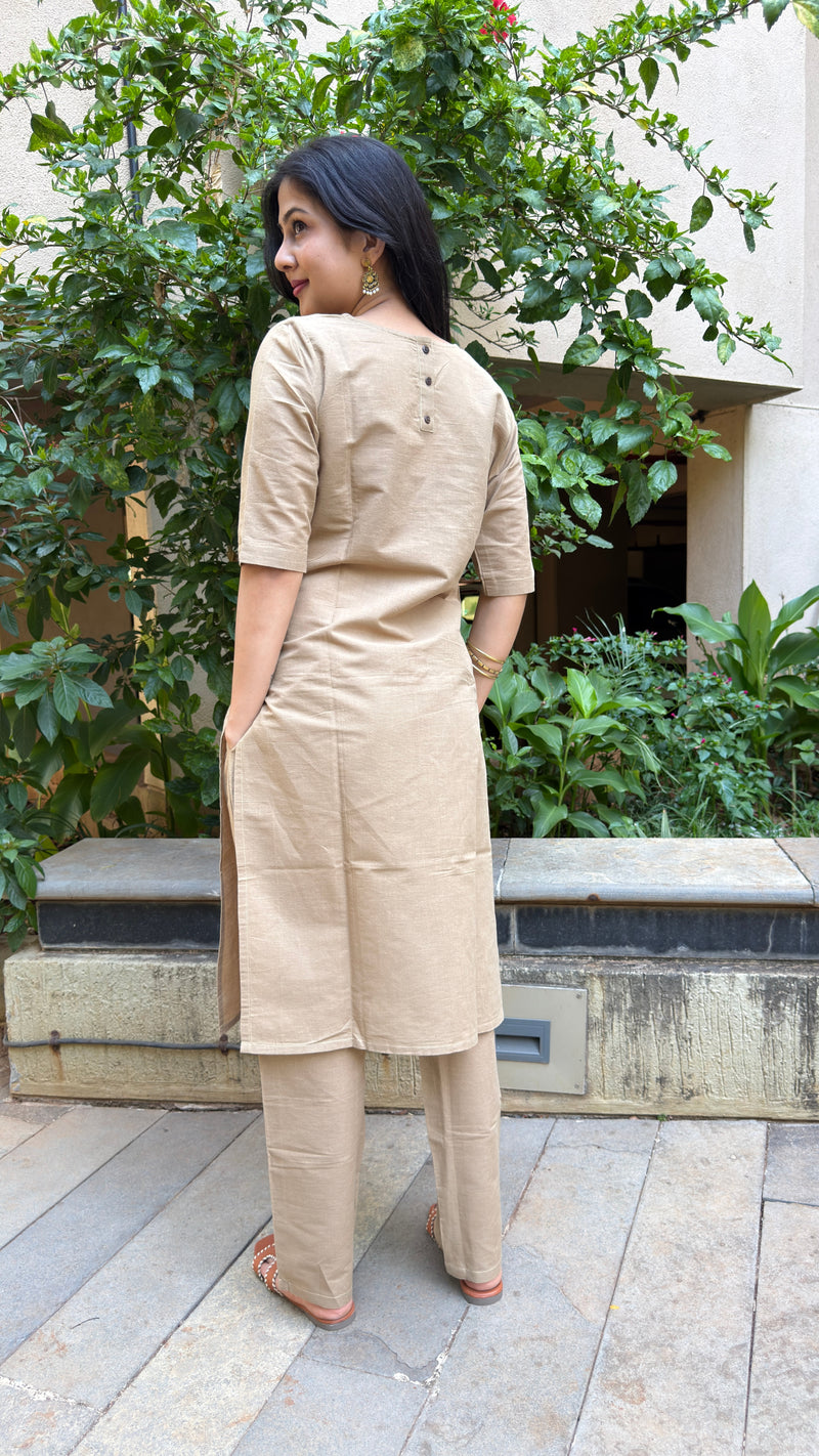A woman wearing a beige cotton kurta set with elbow sleeves, seated outdoors with natural background.