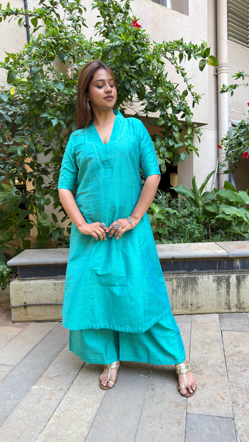 Standing pose of a woman wearing a solid teal kurta set made of slub silk with natural daylight.