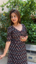 Model in black wrap dress walking through outdoor setting