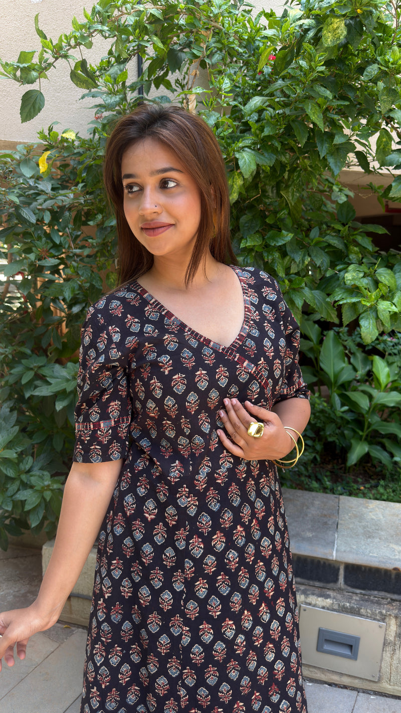 Detail shot of a woman wearing a black cotton long dress, focusing on the printed pattern and sleeve length against an outdoor plant background.