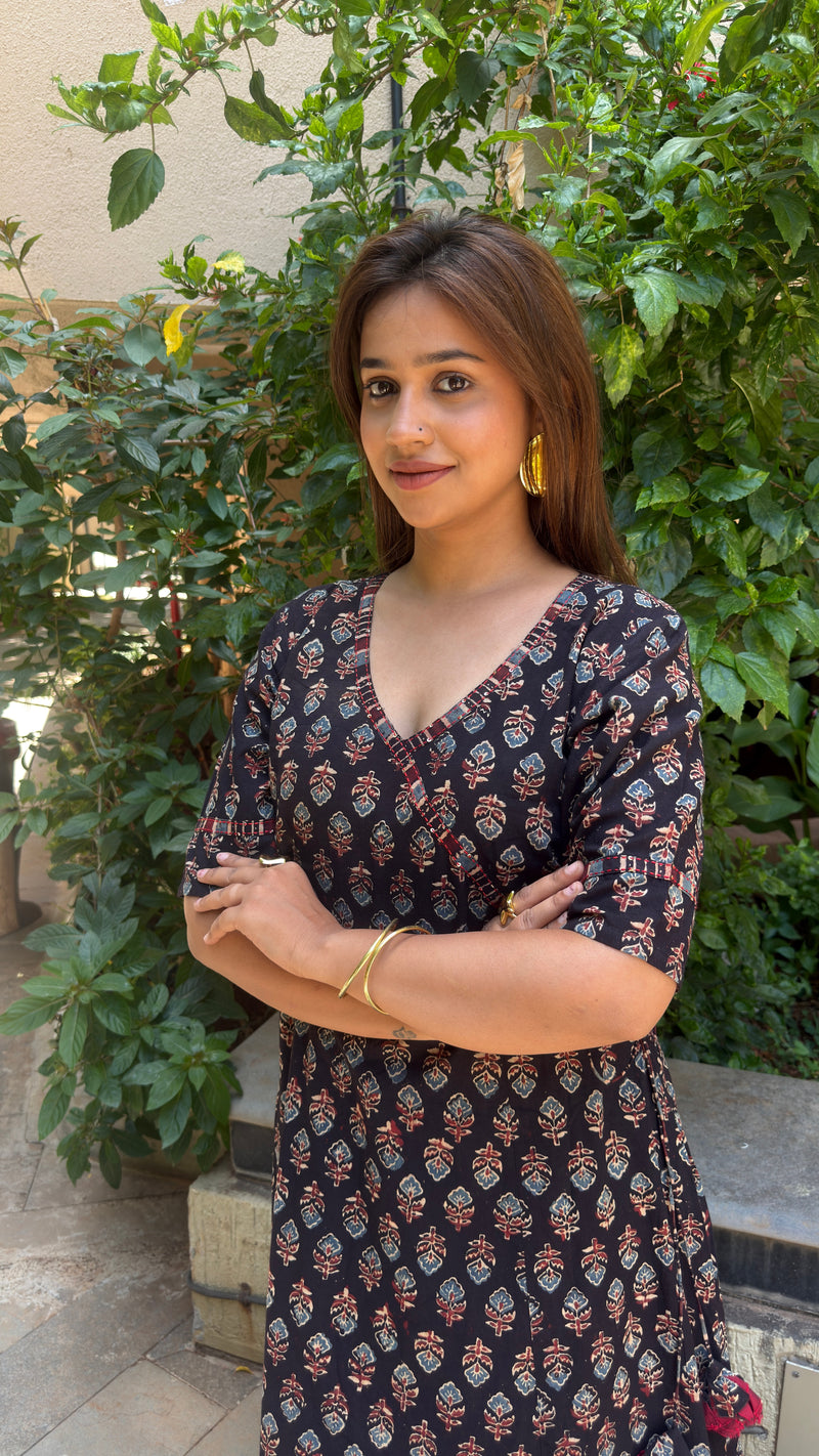 Portrait of a woman wearing a black cotton long dress, capturing the upper body fit, V-wrap neckline, and hand block print details clearly.
