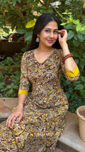 Model seated in olive handloom cotton long dress with dense mustard yellow floral block print, V-neckline and three-quarter sleeves