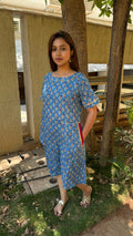 Model walking in blue kaftan calf-length dress through outdoor space
