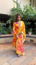 Model in bright yellow organza kurta set with bold pink and orange floral printed dupatta with gold border