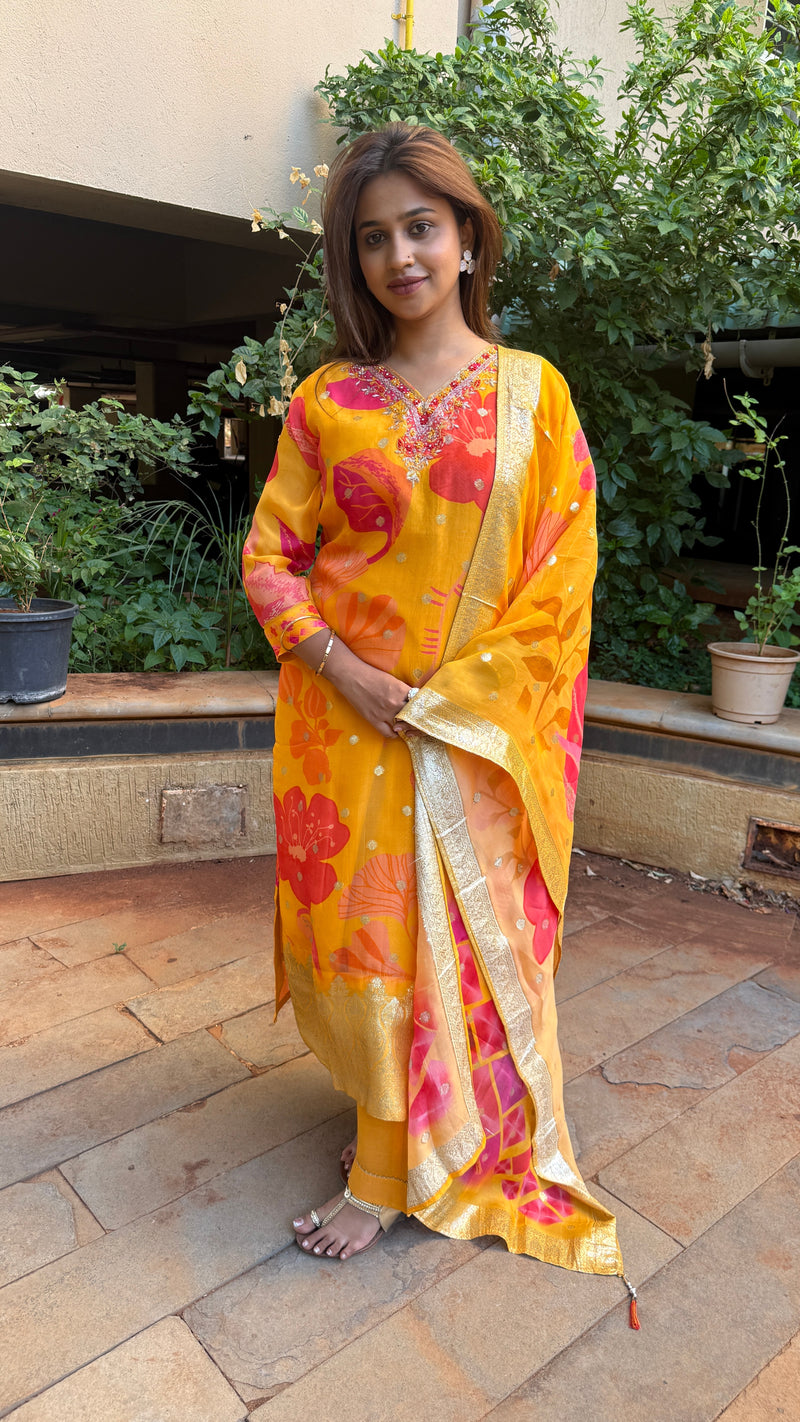 Back view of the yellow floral organza kurta set worn by a woman against a green garden background.
