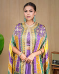 Model posing with hand on hip showcasing the purple fusion cape set and emerald statement jewelry.