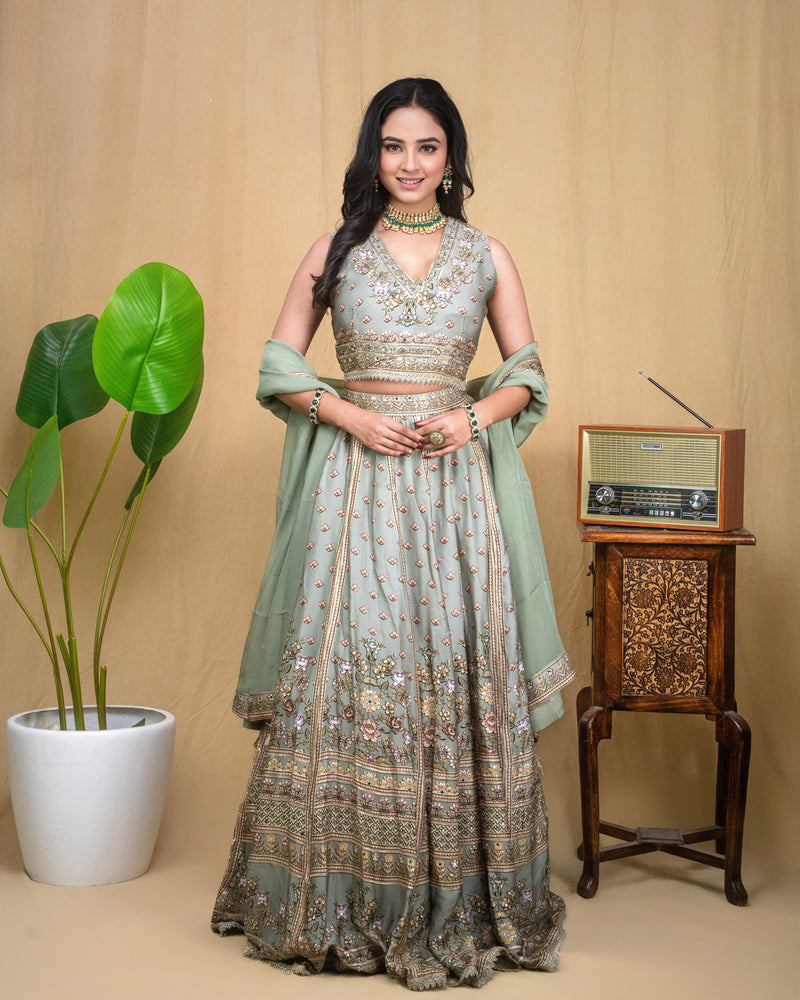 Full length view of a woman in a sage green hand embroidered modal lehenga set with dupatta.