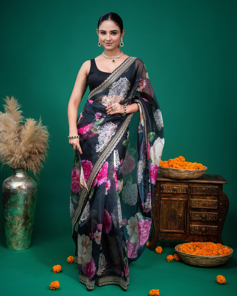 Woman wearing a black floral organza saree with pink flowers and embroidered border